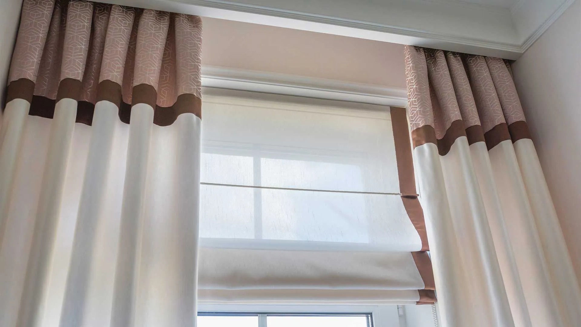 Two-tone drapery panels and a Roman shade framing a window